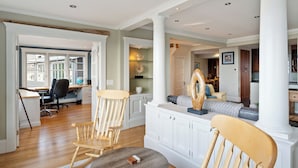 A spacious living room with a wooden rocking chair, a dining area with a table and chairs, and a kitchen area with a desk and computer. - Magnificent Ocean View; Walk to beaches and town (Swampscott)