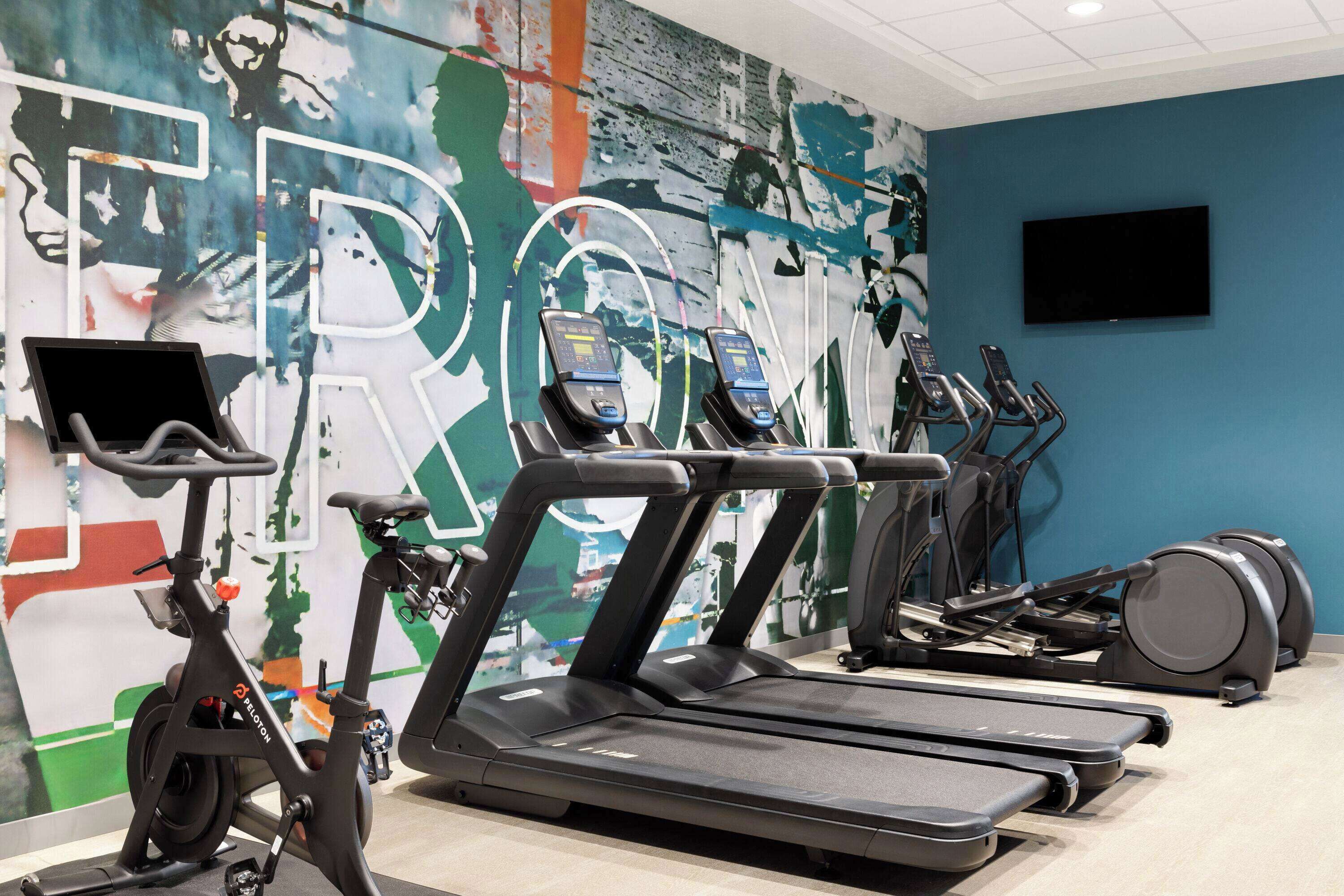 A gym with treadmills, stationary bikes, and a TV on the wall.