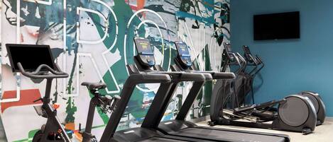 Ein Fitnessstudio mit Laufbändern, Ergometer und einem Fernseher an der Wand.