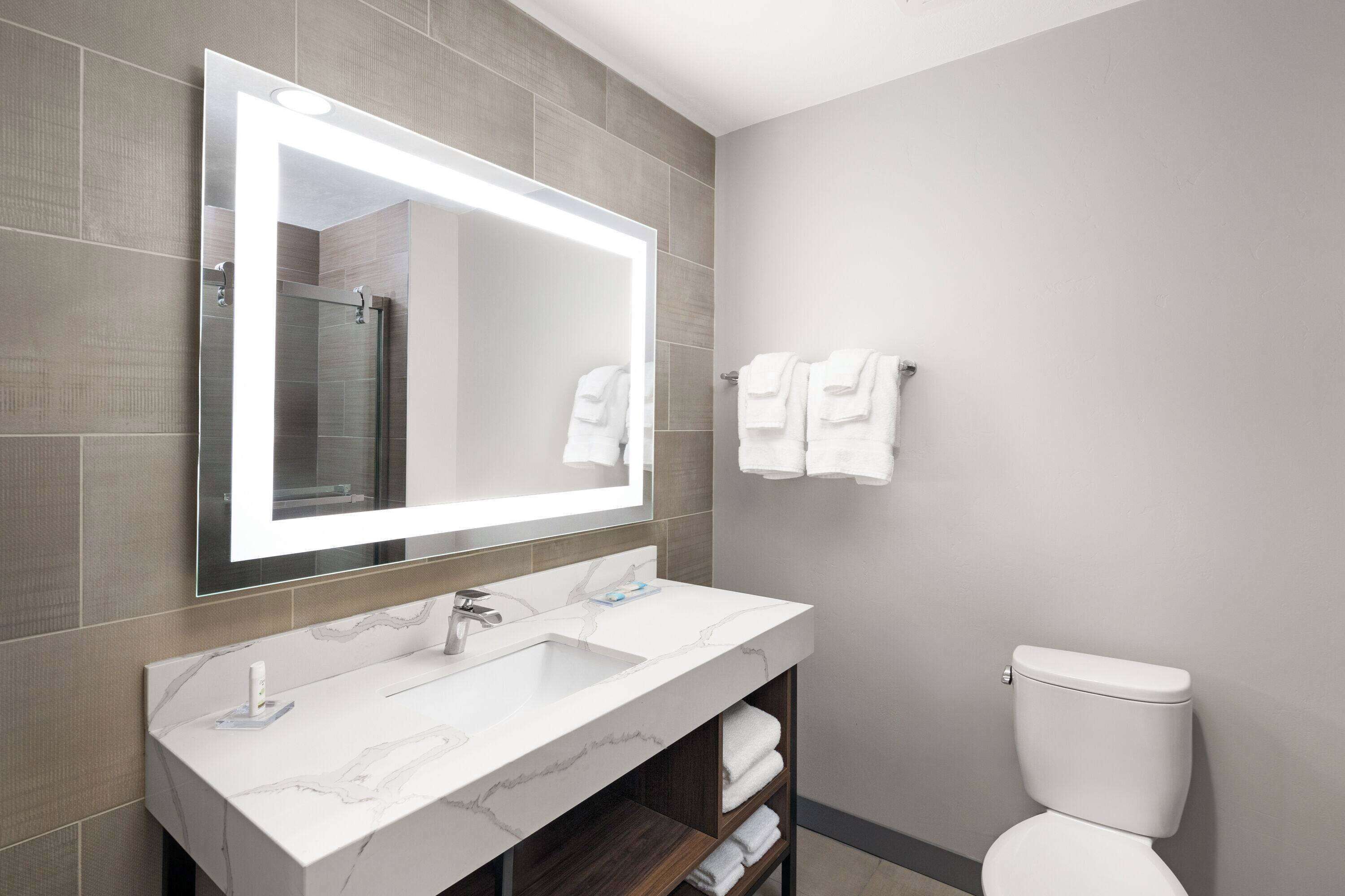 A modern bathroom with a large mirror, a marble sink, and a toilet.