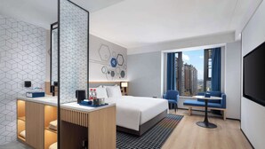 A modern hotel room with a large bed, a desk with a mirror, a seating area with a sofa and chairs, and a large window offering a city view. - Microtel By Wyndham Changsha South Railway Station (Changsha)