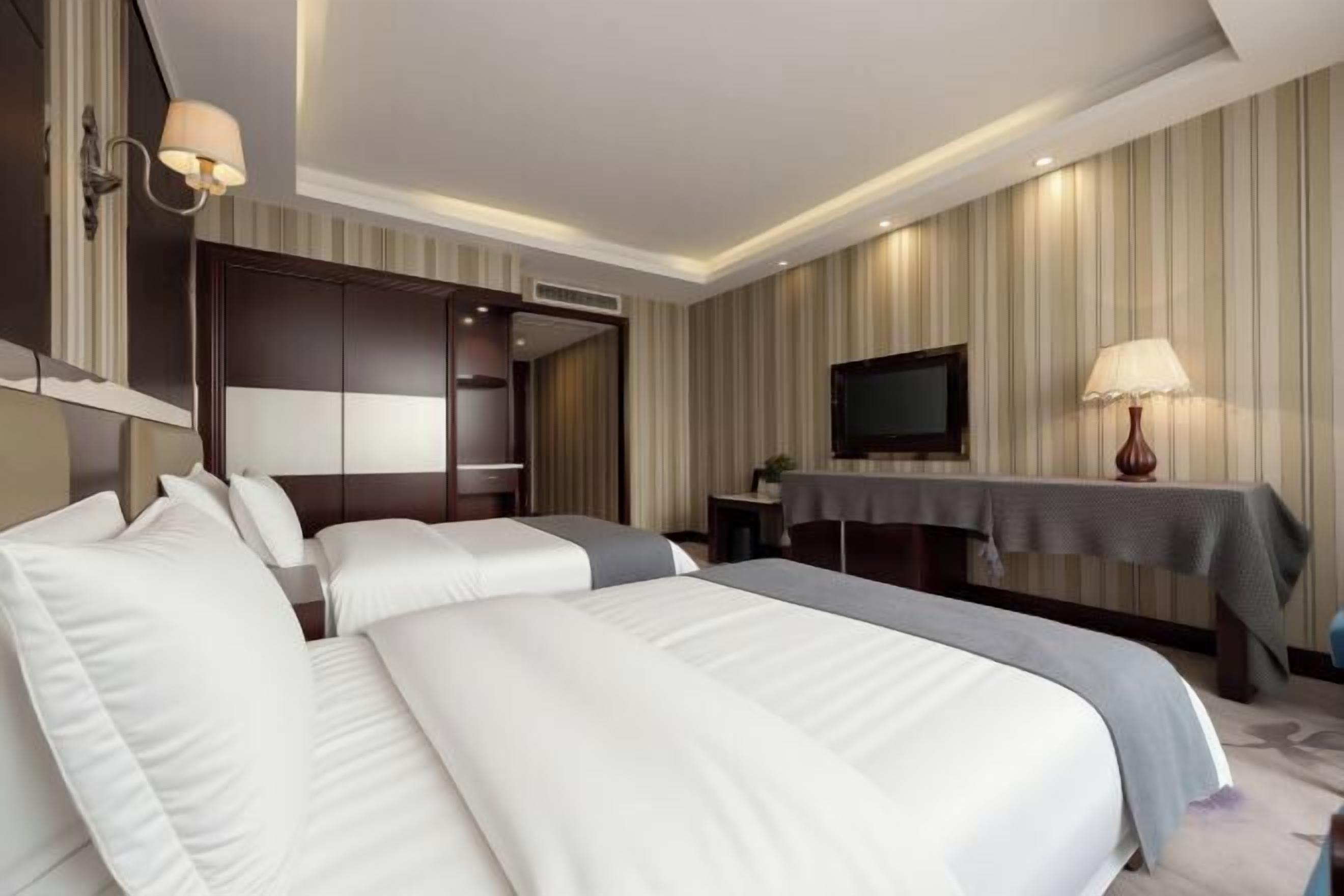 A hotel room with two beds, a TV, a desk, and a lamp.