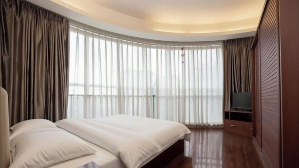 Una habitación de hotel moderna con techo curvo, una cama grande, televisor de pantalla plana y vistas a la ciudad a través de amplios ventanales.