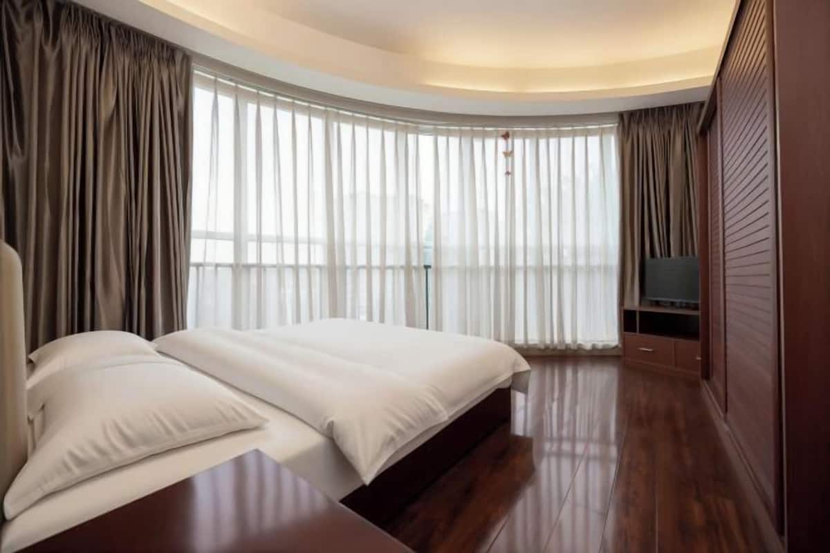 Una habitación de hotel moderna con techo curvo, una cama grande, televisor de pantalla plana y vistas a la ciudad a través de amplios ventanales.