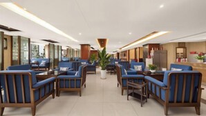 Un vestíbulo de hotel con zonas de estar, un mostrador de recepción y una planta grande en maceta.