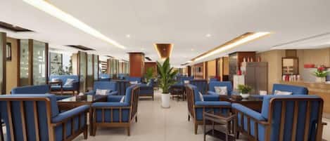 Un hall d’hôtel avec des espaces aménagés pour s’asseoir, un comptoir d’accueil et une plante au centre.