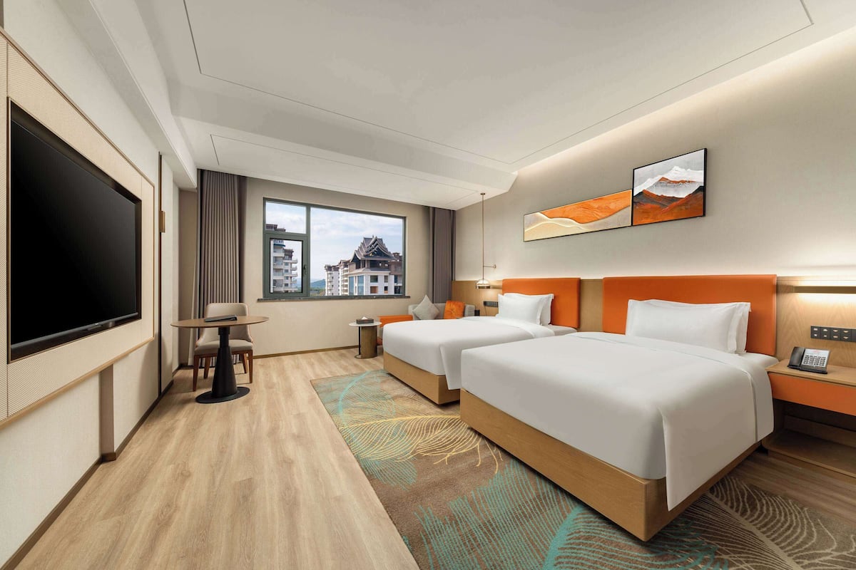 Een hotelkamer met twee bedden, een televisie, een tafeltje en een raam met uitzicht op gebouwen.