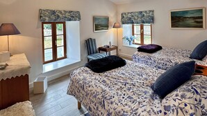 A bedroom with a large bed, two windows with curtains, a chair, a lamp, and a view of the outdoors. - Charming 2-bedroom Gite in peaceful Niort - WiFi, 10 mins from City Center (Niort)