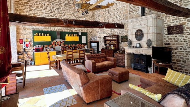 A rustic interior with exposed wooden beams, a stone wall, a kitchen area, and a cozy seating arrangement. - Charming 2-bedroom Gite in peaceful Niort - WiFi, 10 mins from City Center (Niort)