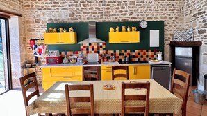 A rustic kitchen with stone walls, yellow cabinets, and a dining area with wooden chairs and a patterned tablecloth. - Charming 2-bedroom Gite in peaceful Niort - WiFi, 10 mins from City Center (Niort)