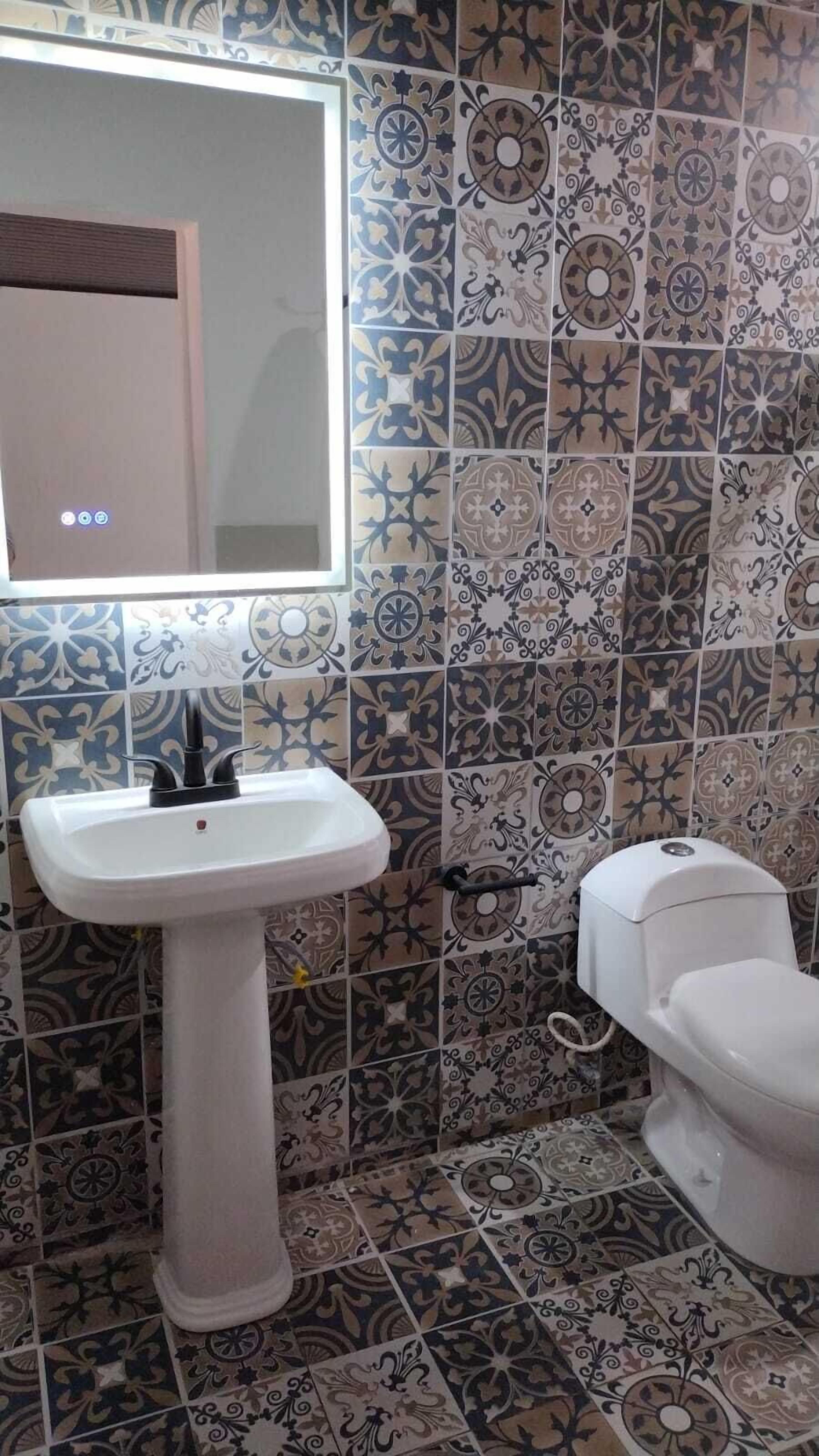 Un baño con un lavamanos blanco de pedestal, un inodoro y una pared con azulejos estampados.