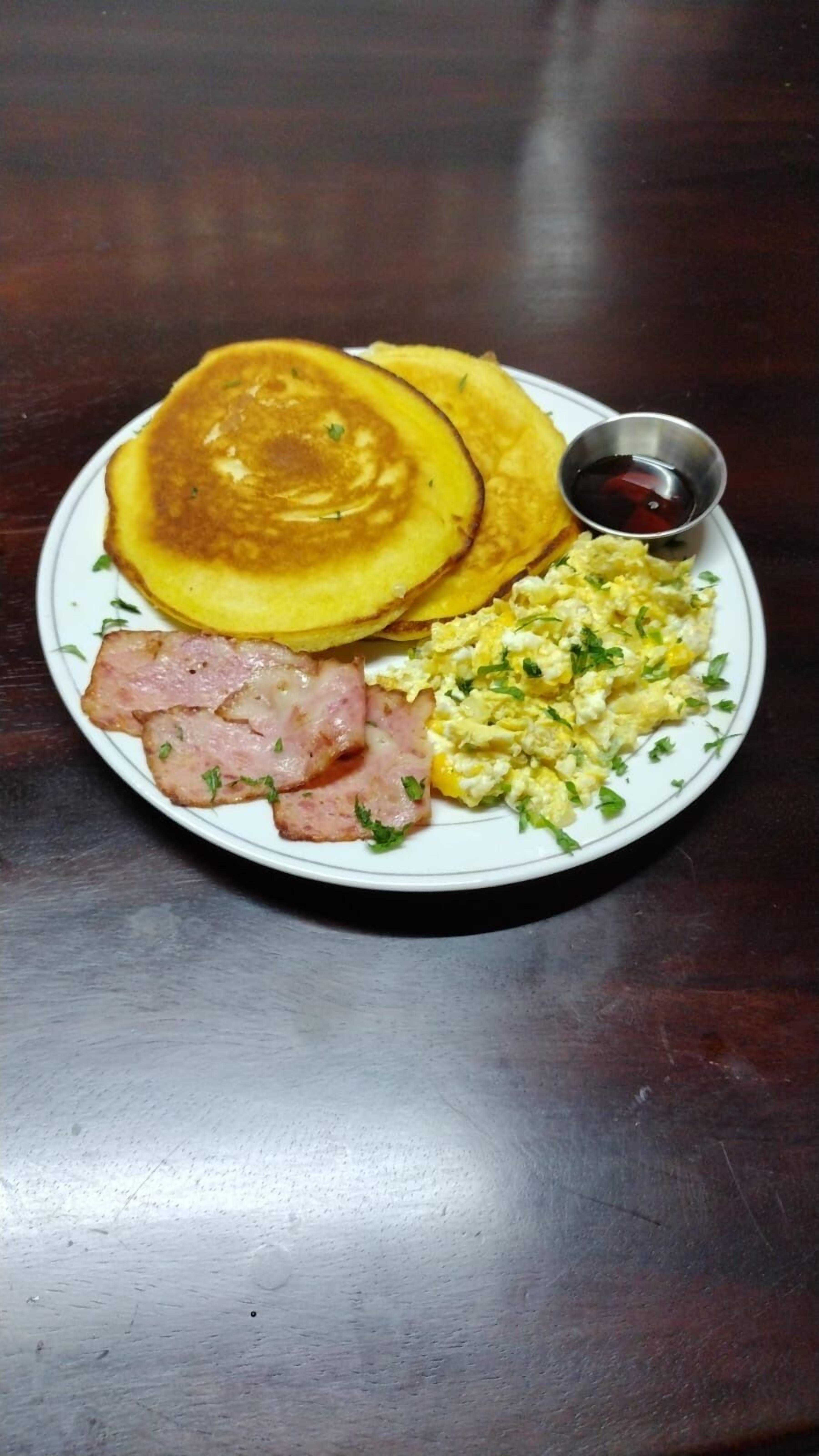 A plate with pancakes, scrambled eggs, and sliced ham.