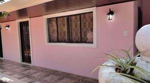 Fachada de un edificio rosa con una ventana estampada, una puerta y dos luces fijadas a la pared.