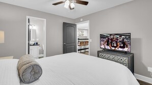 Ein Schlafzimmer mit einem Bett, einem Deckenventilator, einem Fernseher und einer Tür zu einem Badezimmer.