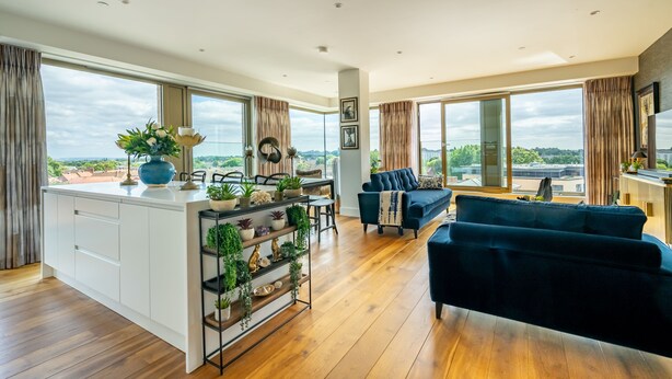 Un salón amplio con un gran ventanal, un sofá azul oscuro y suelo de madera.