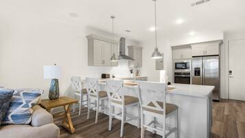 Una cocina moderna con armarios blancos, un refrigerador de acero inoxidable y una isla central con taburetes de bar.