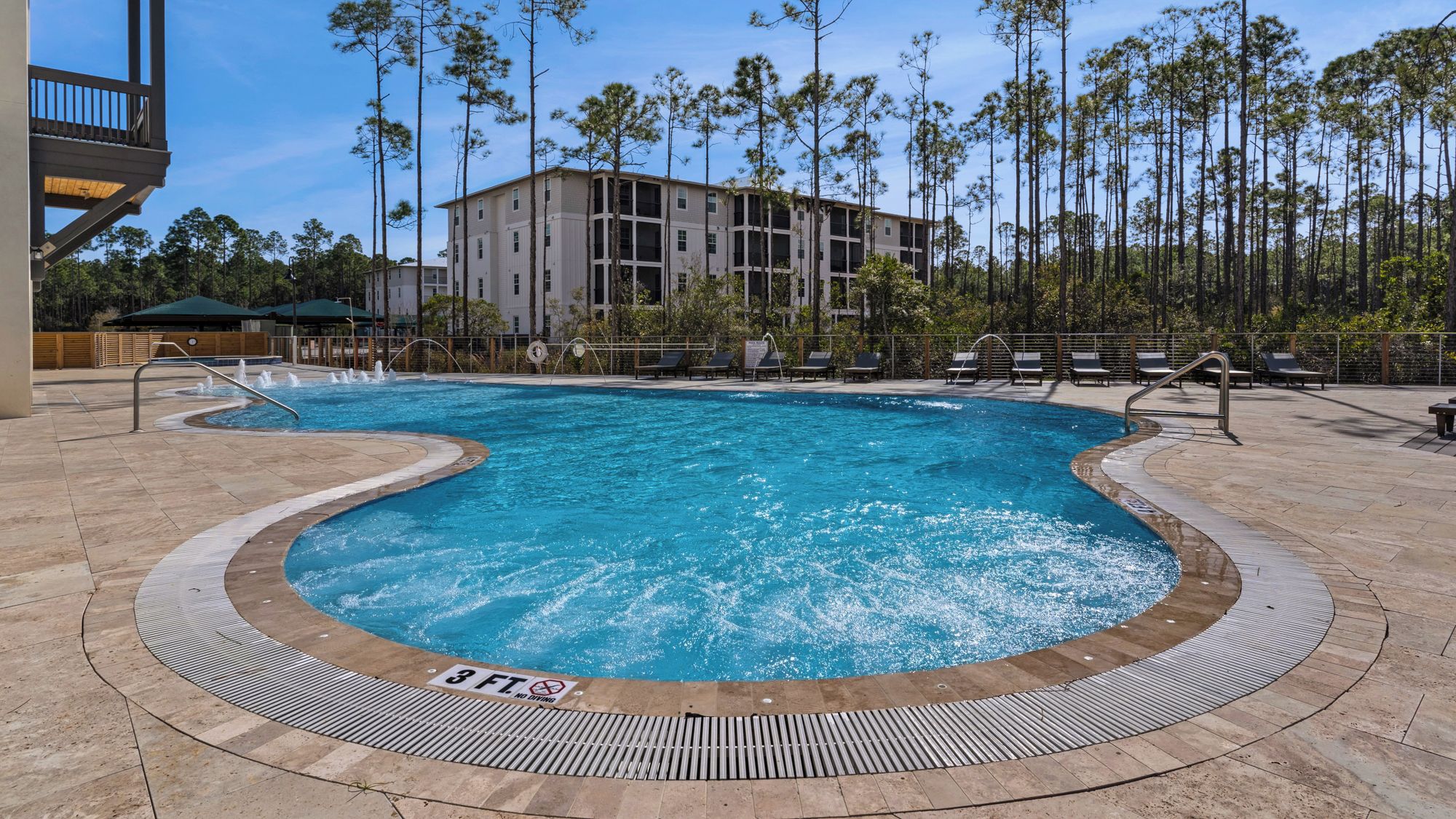 A swimming pool with a 3 FT no diving sign, surrounded by lounge chairs and a building in the background.