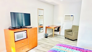 A hotel room with a bed, a TV on a wooden cabinet, a desk with a chair, a striped armchair, and a mirror. - Brant Inn (Brantford)