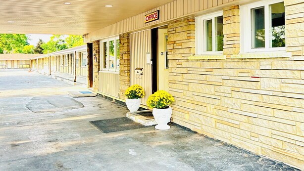 A motel with a row of rooms under a covered walkway, a 'No Parking' sign, and two potted plants on the sidewalk. - Brant Inn (Brantford)