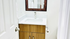 A bathroom with a white vanity, a wooden cabinet, a mirror, and a shower curtain. - Brant Inn (Brantford)