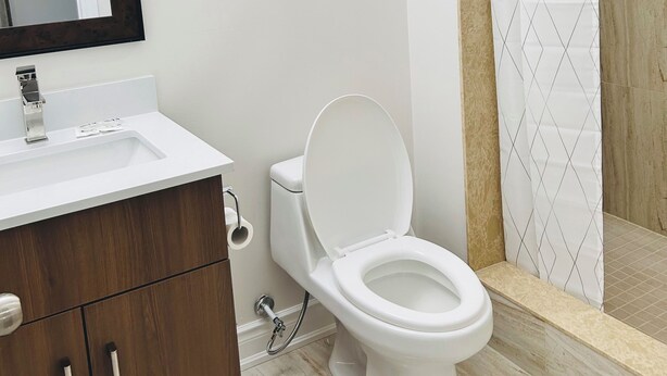 Une salle de bain moderne avec un lavabo blanc, des toilettes, une douche dotée d’un rideau à motifs losangés et un miroir avec un cadre en bois.