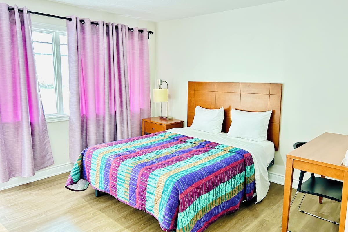 A hotel room with a bed, a nightstand, a lamp, and a window with curtains.