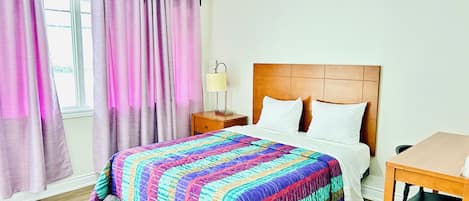 A hotel room with a bed, a nightstand, a lamp, and a window with curtains.