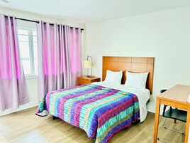 Una habitación de hotel con cama, mesita de noche, lámpara y ventana con cortinas.