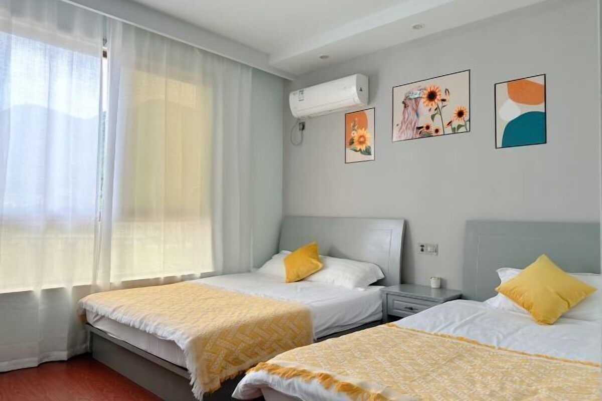 A hotel room with two beds, a window with sheer curtains, an air conditioning unit, and wall art.