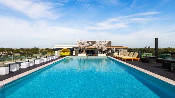 Une piscine sur le toit, avec une eau d’un bleu cristallin, entourée de chaises longues blanches et d’un ponton jaune flottant.