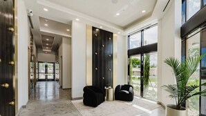 Un hall d’entrée moderne avec un sol en marbre, des fauteuils noirs à revêtement en tissu, une grande plante en pot et une vue à travers les portes vitrées.