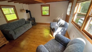 A cozy room with a wooden floor, two sofas, a fireplace, and large windows.