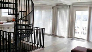 Un interior moderno con una escalera espiral, un balcón con cortinas y vistas a la ciudad.