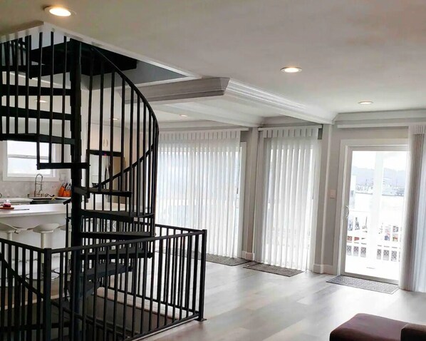 A modern interior with a spiral staircase, a balcony with curtains, and a view of the city.
