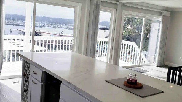 Una cocina moderna con una isla grande, armarios blancos y vistas a un puerto deportivo a través de amplios ventanales.