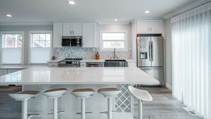 Una cocina moderna con gabinetes blancos, electrodomésticos de acero inoxidable, una isla de mármol y taburetes de bar.
