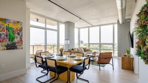 Un salón amplio con un ventanal grande, un comedor con mesa y sillas de madera, un sofá y un televisor montado en la pared.