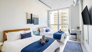 Habitación de hotel con dos camas, televisión, ventana con vista a la ciudad y alfombra azul estampada.
