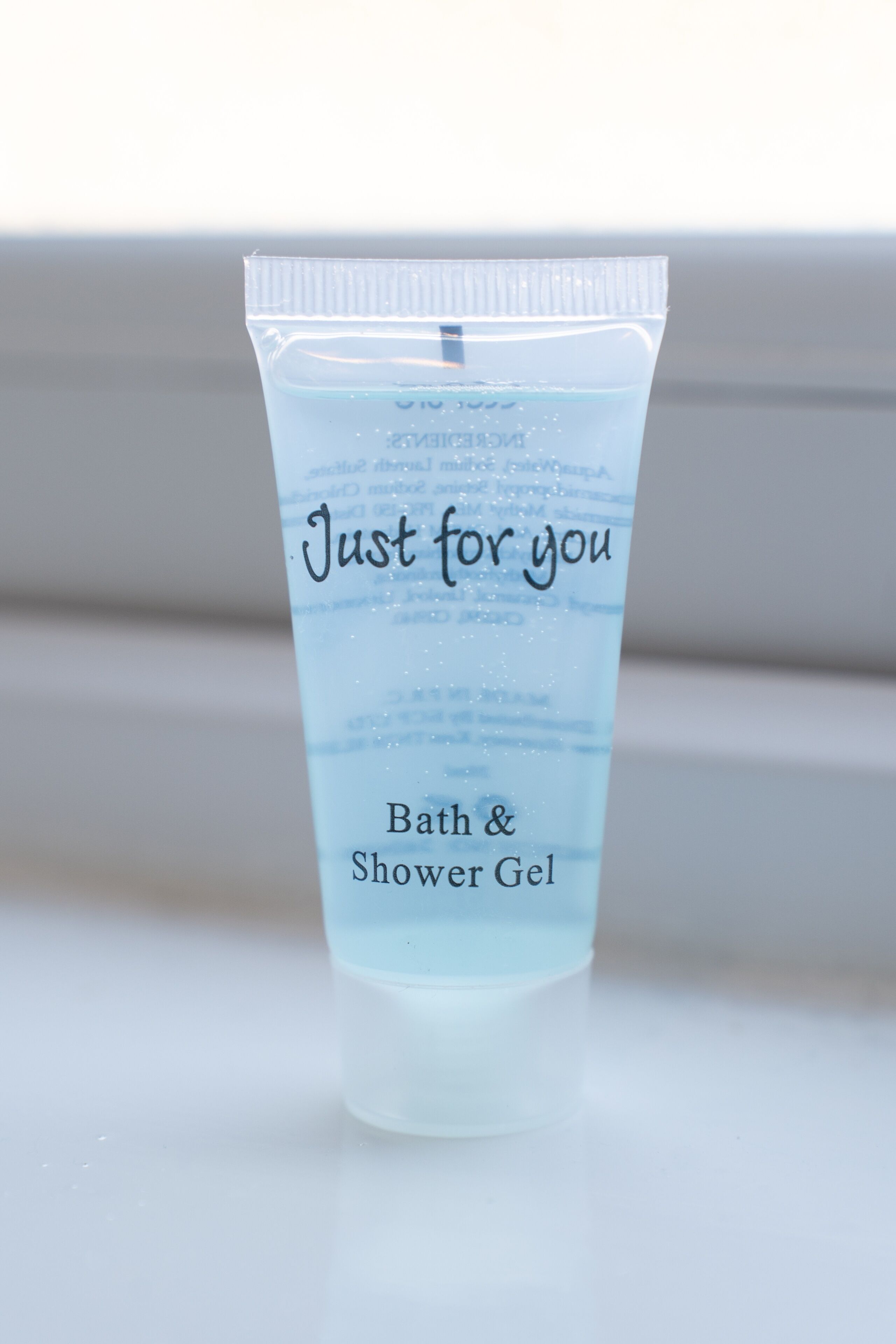 Un tubo transparente de gel de baño y ducha con el rótulo 'Just for you' sobre una superficie blanca.