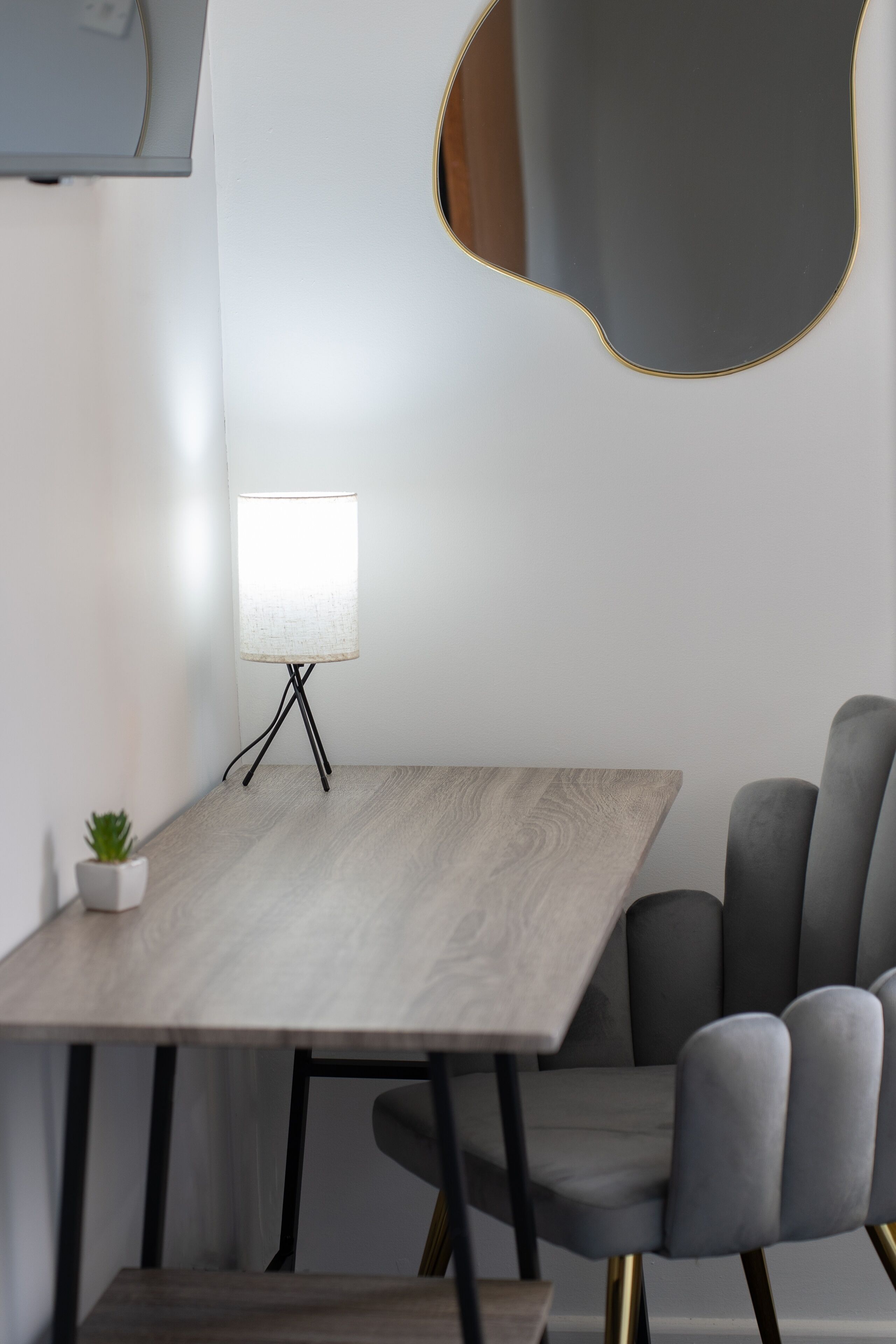 A modern dining area with a wooden table, a lamp, and a grey upholstered chair.