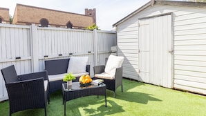 An outdoor patio with wicker furniture, a table with a plant and fruit, and a white shed in the background. - Open Mind Property - 4 Beds 2 Bathrooms & Parking (Portsmouth)