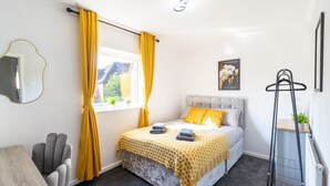 A bedroom with a bed, a desk, a chair, a window with yellow curtains, a painting, and a radiator. - Open Mind Property - 4 Beds 2 Bathrooms & Parking (Portsmouth)