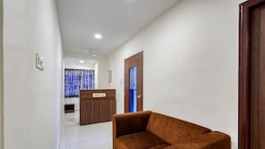 A hotel reception area with a reception desk, a sofa, and a door. - Eco Stay Mount Road (Chennai)