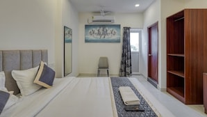 A hotel room with a bed, a chair, a wardrobe, and a painting on the wall. - Eco Stay Mount Road (Chennai)