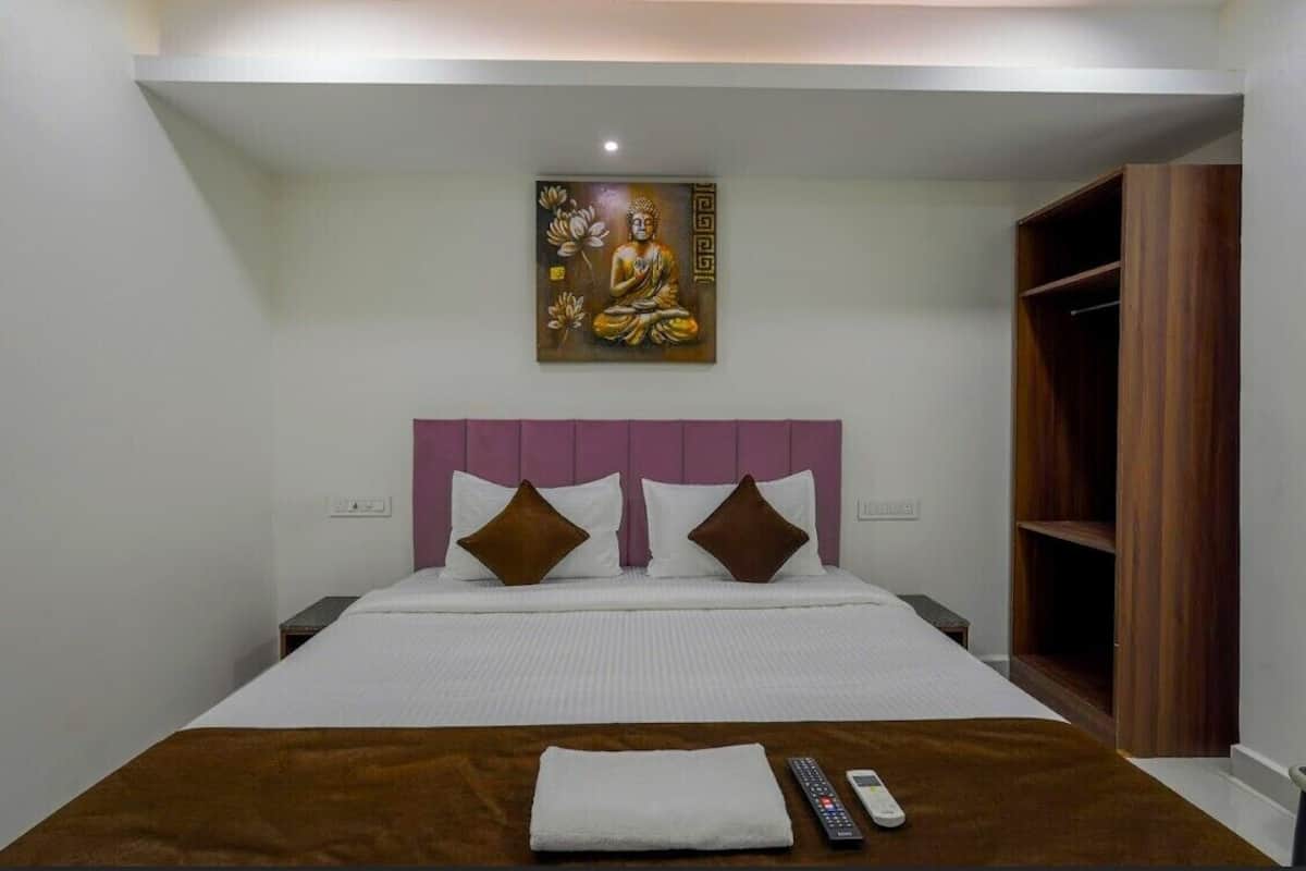 Une chambre d’hôtel avec un lit, une tête de lit, un tableau, une armoire et une télécommande posée sur le lit.