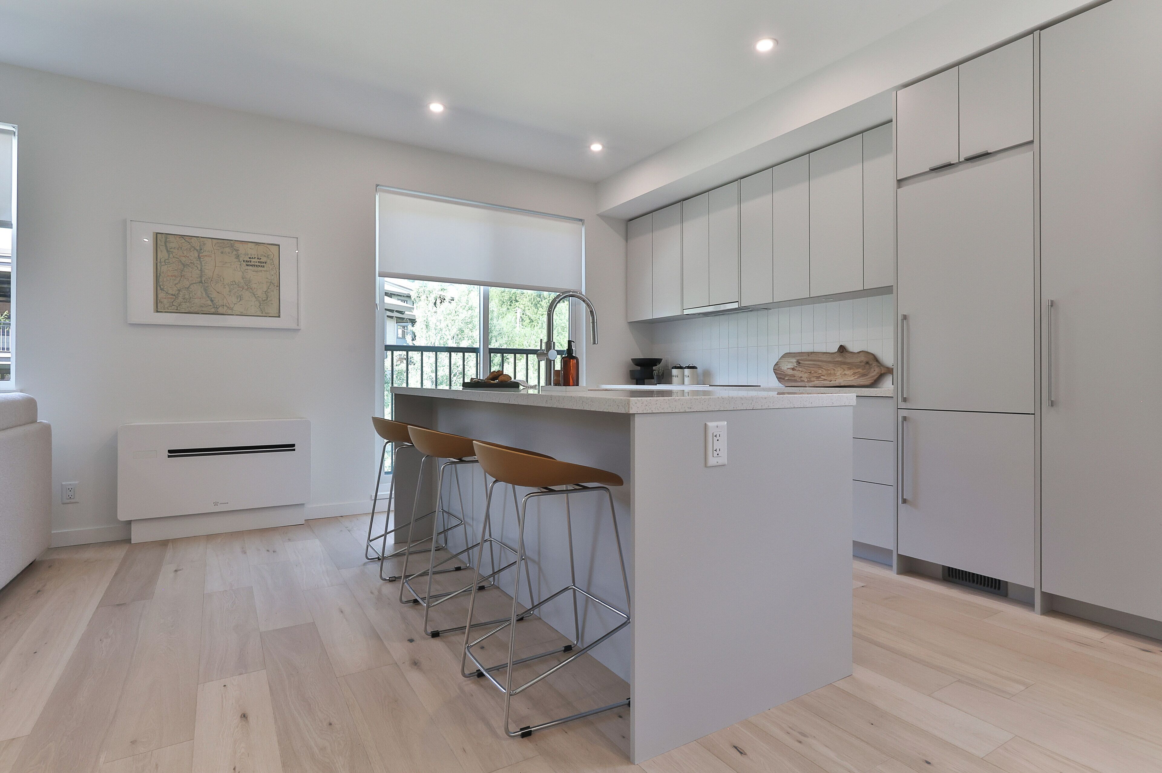 A modern kitchen with a central island, bar stools, and a large window.