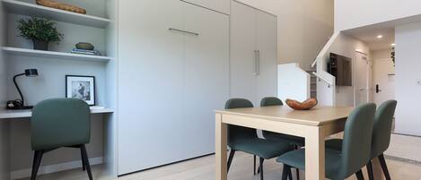 Een moderne eethoek met een houten tafel en vier stoelen, een boekenkast met decoratieve items, en een trap die naar een ander niveau leidt.