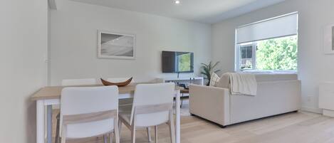 Una sala de estar moderna con comedor, sofá, televisor y un ventanal grande.