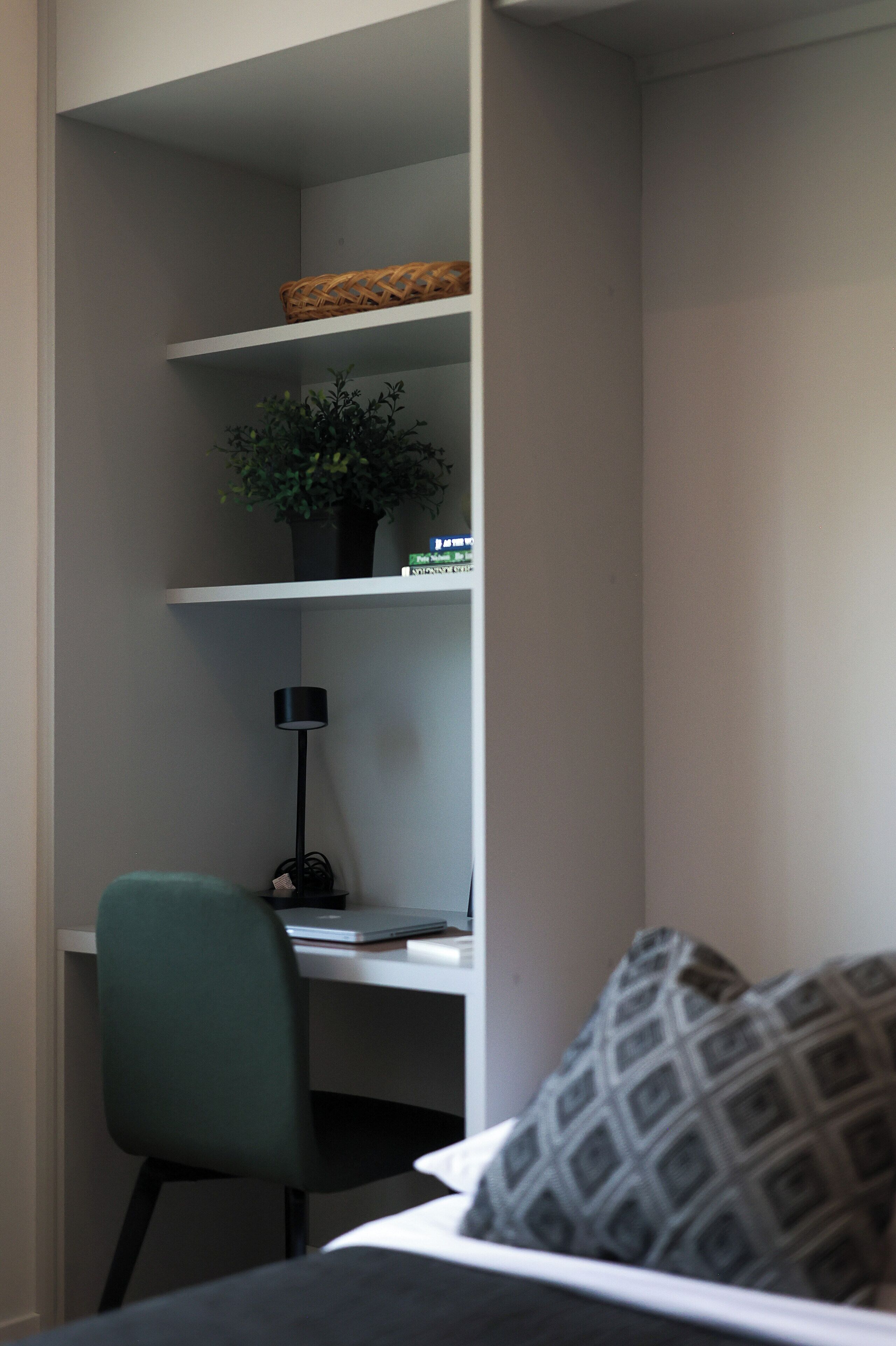 A room with a desk, a chair, a lamp, a plant, and a shelf with a basket.