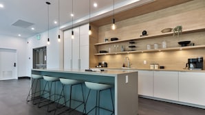 A modern kitchen with a central island, bar stools, wooden shelves, and a coffee machine. - The Crescent (Rossland)